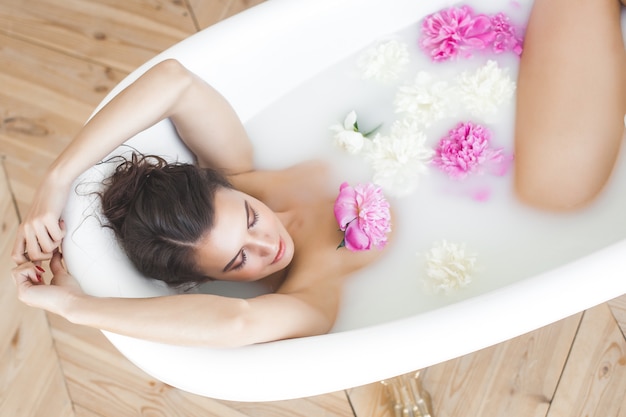 Belle jeune femme prenant un bain avec des fleurs et du lait