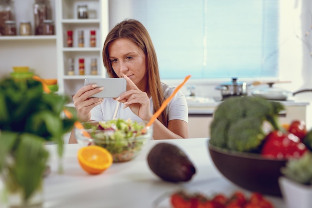 Belle jeune femme prenant une photo de salade saine avec un smartphone pour son blog.