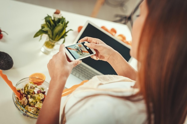 Belle jeune femme prenant une photo de salade saine avec un smartphone pour son vlog.