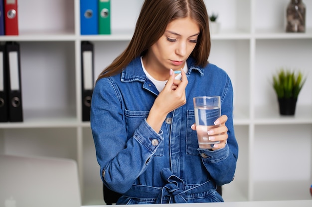 Belle jeune femme prenant la pilule au bureau.