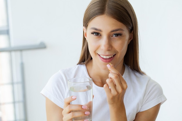 Belle jeune femme prenant une pilule d'huile de poisson jaune