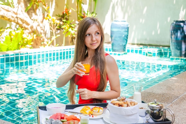 Belle jeune femme prend son petit-déjeuner dans une piscine privée sur une villa dans un complexe de luxe