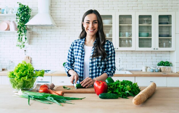 Belle jeune femme prépare une salade de légumes dans la cuisine. Nourriture saine. Salade végétalienne. Diète. Concept de régime. Mode de vie sain. Cuisiner à la maison. Préparer la nourriture. Ingrédients de coupe sur la table