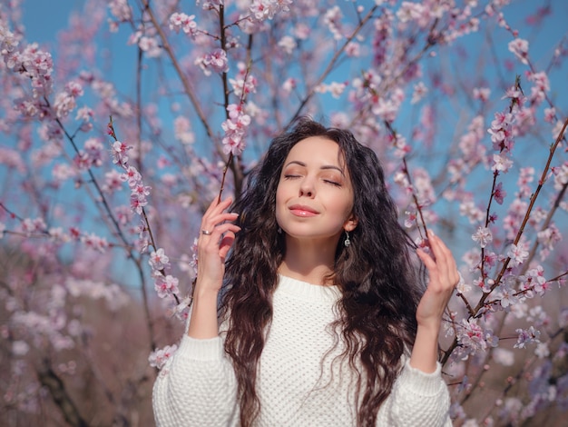 Une belle jeune femme près d'un cerisier de printemps en fleurs. L'idée et le concept de soins personnels, de santé et de bonheur