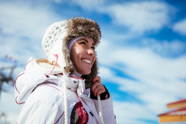 Belle jeune femme profitant de vacances au ski. Elle pose le jour d'hiver ensoleillé et regarde au loin avec le sourire.