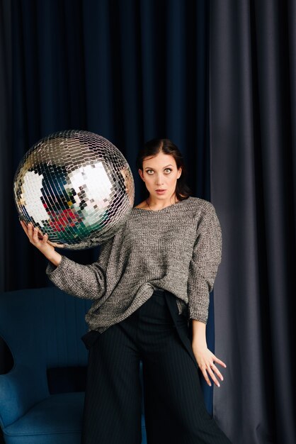 Belle jeune femme en pull gris et boule disco à la maison