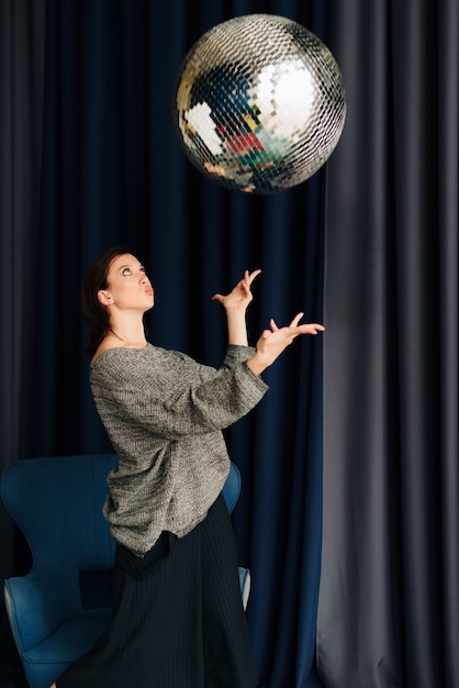 Belle jeune femme en pull gris et boule disco à la maison