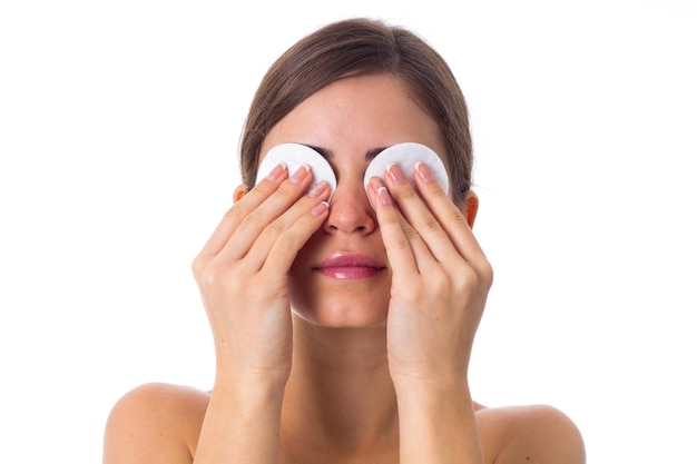 Belle jeune femme avec queue de cheval fermant les yeux par des tampons de coton sur fond blanc en studio