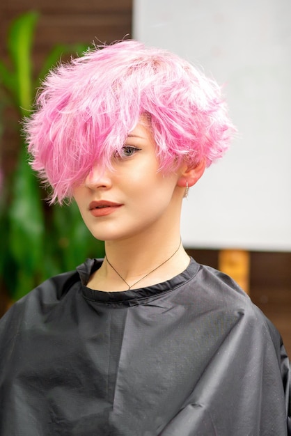 La belle jeune femme de race blanche avec une nouvelle coiffure courte rose dans le reflet du miroir en regardant la caméra dans un salon de coiffure