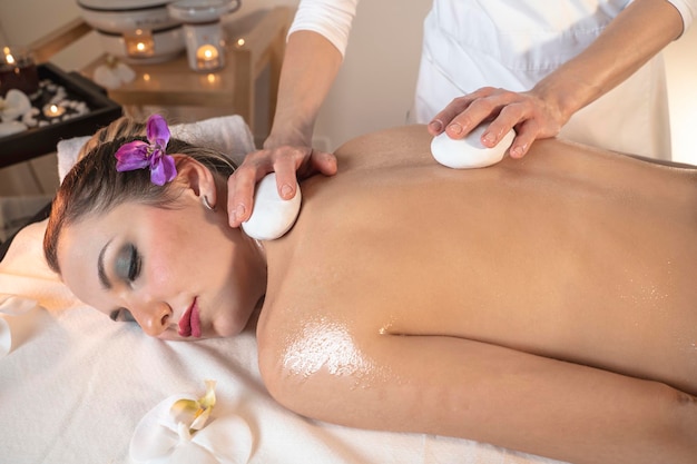 Belle jeune femme recevant un massage aux pierres chaudes dans un salon de spa