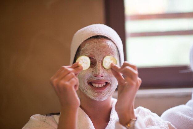 Belle jeune femme reçoit un masque facial à l'argile au spa, allongée avec des concombres sur les yeux