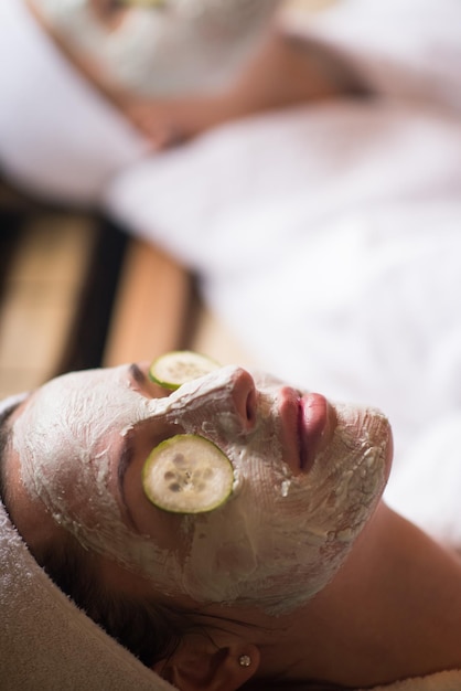 Belle jeune femme reçoit un masque facial à l'argile au spa, allongée avec des concombres sur les yeux