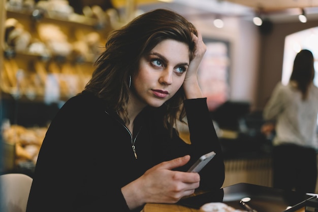 Belle jeune femme réfléchie avec mobile au restaurant