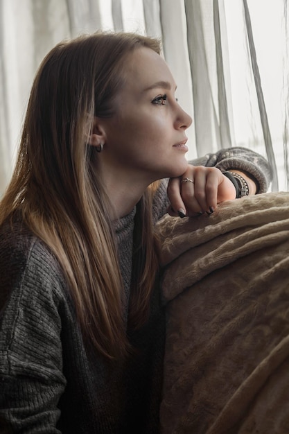 belle jeune femme regarde pensivement et rêveusement par la fenêtre à la maison