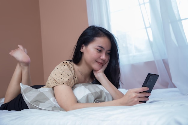 Belle jeune femme relaxante sur le lit tout en tenant un téléphone portable