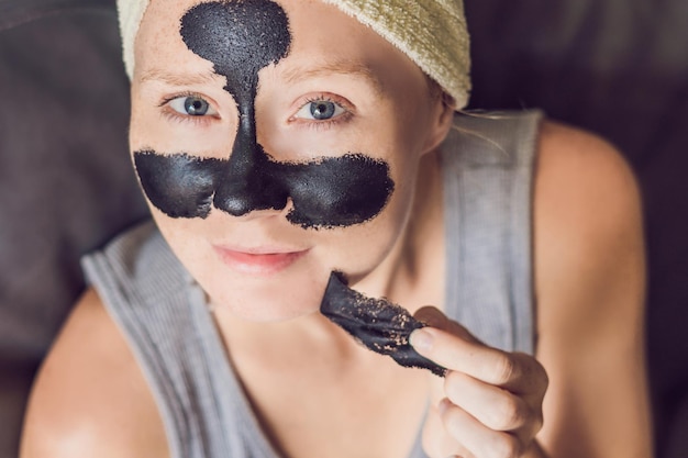 Belle jeune femme relaxante avec masque facial au spa de beauté. Heureuse femme joyeuse appliquant un masque noir sur le visage.