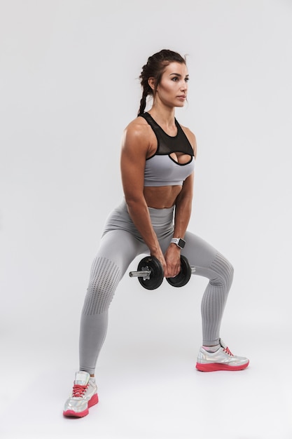 belle jeune femme de remise en forme sportive forte incroyable posant isolée sur fond de mur blanc faire des exercices avec haltère.