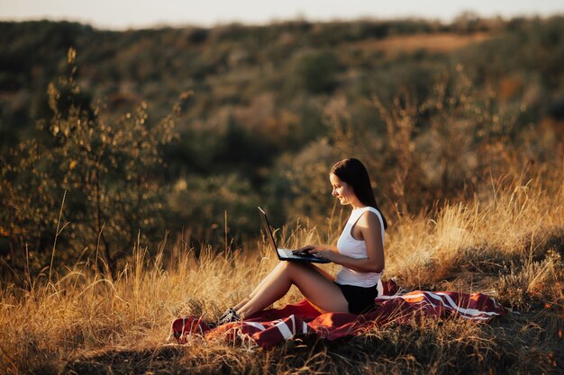 Belle jeune femme reposante sur l'herbe avec ordinateur portable.