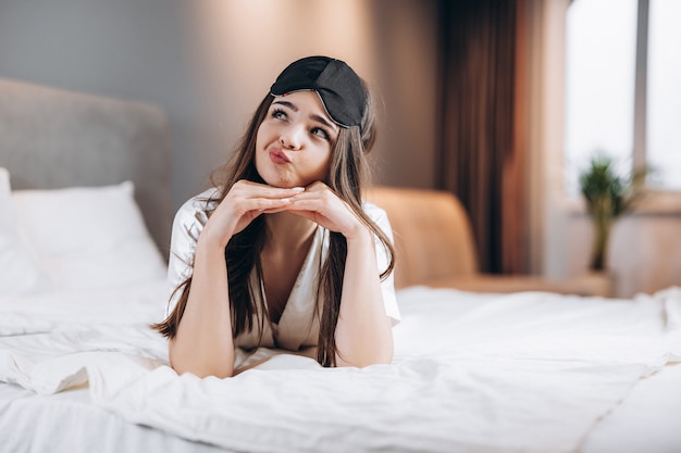 Belle jeune femme rêvant en position allongée sur le lit. Un modèle féminin aux cheveux bruns et aux beaux yeux pense à quelque chose d'intéressant. matin ou soir dans la chambre avec un modèle féminin.