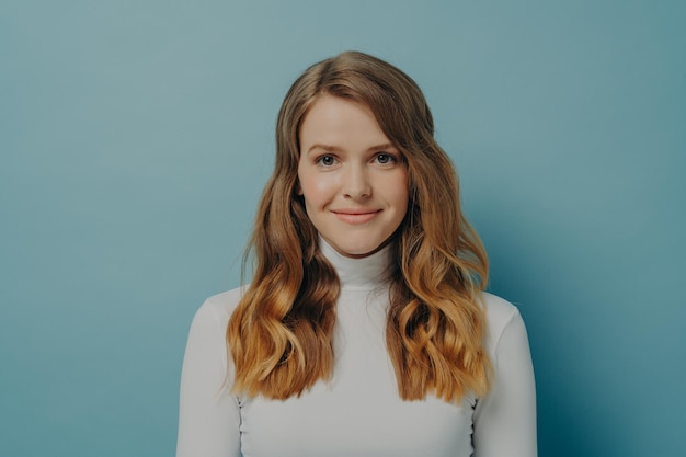 Photo belle jeune femme rêveuse aux cheveux parfaitement ondulés en col roulé blanc souriant à la caméra