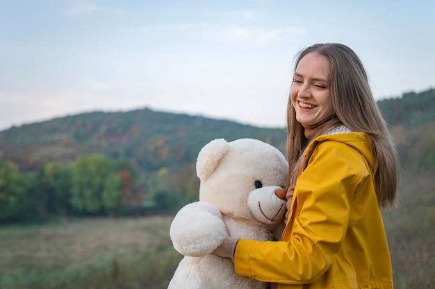 Belle jeune femme riante avec ours en peluche le jour de l'automne Heureuse jeune femme en parka jaune se promène dans la nature