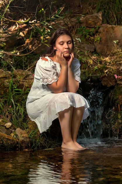 Belle jeune femme avec une robe blanche près du jet d'eau.