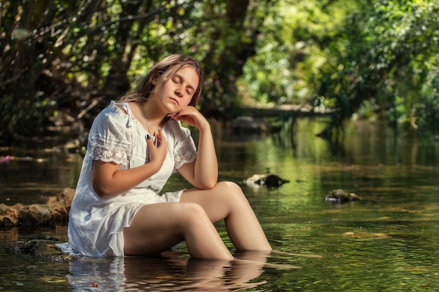 Belle jeune femme avec une robe blanche près du jet d'eau.