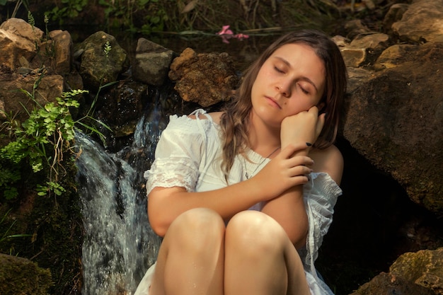 Belle jeune femme avec une robe blanche près du jet d'eau.