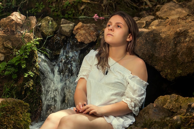 Belle jeune femme avec une robe blanche près du jet d'eau.