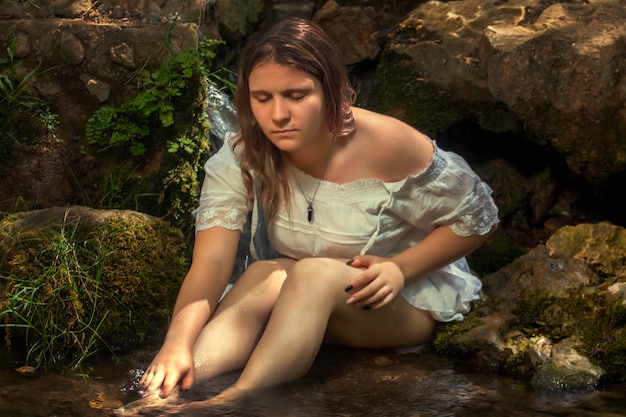 Belle jeune femme avec une robe blanche près du jet d'eau.