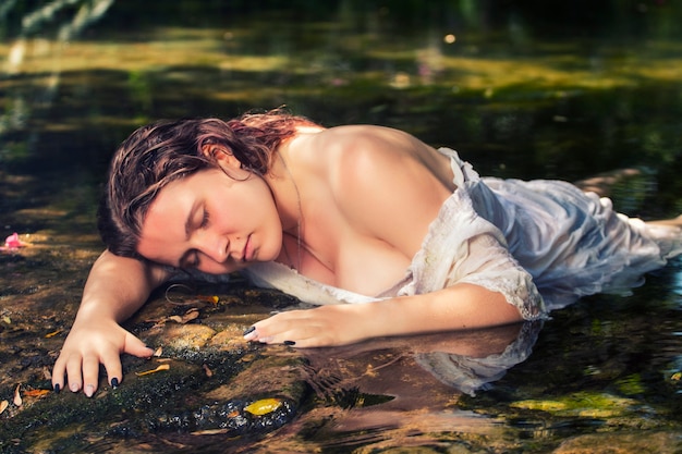 Belle jeune femme avec une robe blanche près du jet d'eau.