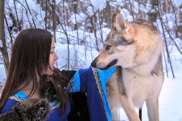 Belle jeune femme en robe bleue communique avec un loup dans une forêt enneigée