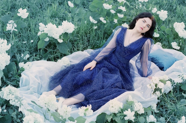 Belle jeune femme en robe bleue sur l'herbe avec des fleurs blanches