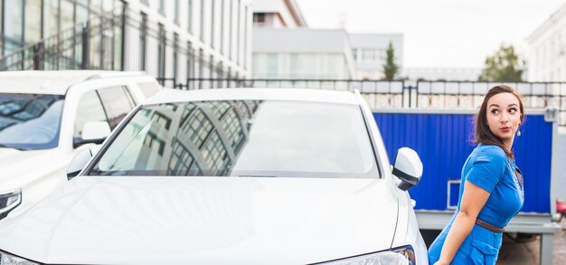 Belle jeune femme en robe bleue posant près de voiture