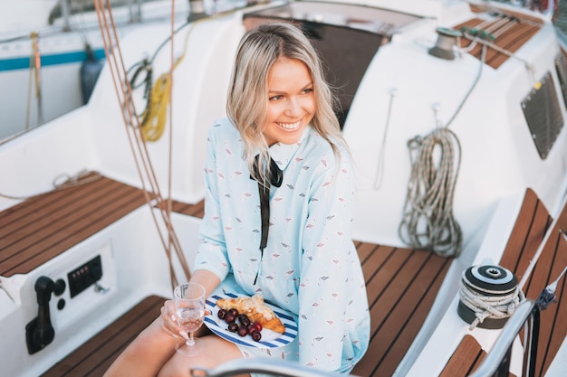 Belle jeune femme en robe bleue avec un verre de soda et de cerise sur le bateau à l'embarcadère au coucher du soleil