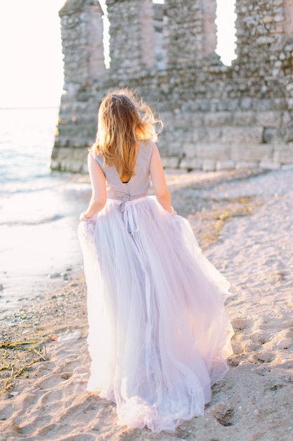 Belle jeune femme en robe élégante bleue marchant près du lac de Garde et de la forteresse de Sirmione, Italie. Belle promenade à Sirmione