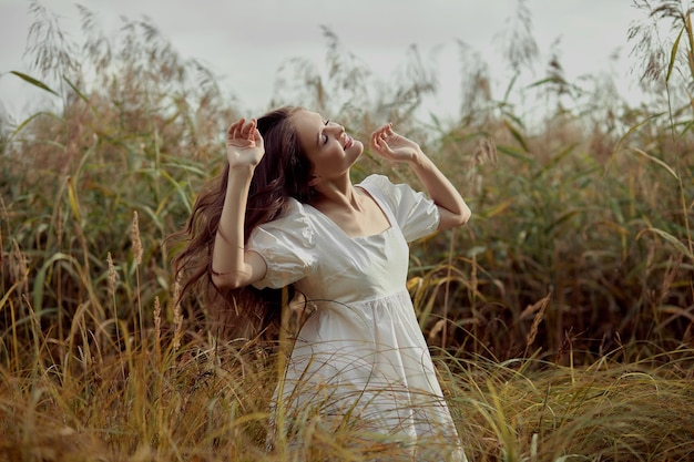 Belle jeune femme en robe d'été blanche est assise dans les hautes herbes dans un champ rural