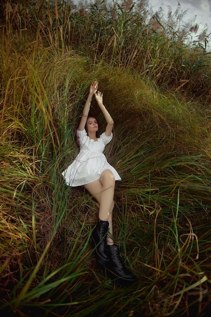 Belle jeune femme en robe d'été blanche est assise dans les hautes herbes dans un champ rural