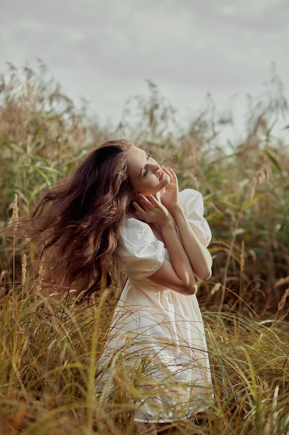 Photo belle jeune femme en robe d'été blanche est assise dans les hautes herbes dans un champ rural