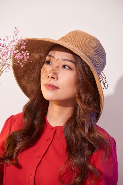 Une belle jeune femme en robe d'été et chapeau de paille posant tout en tenant des fleurs de bouquet
