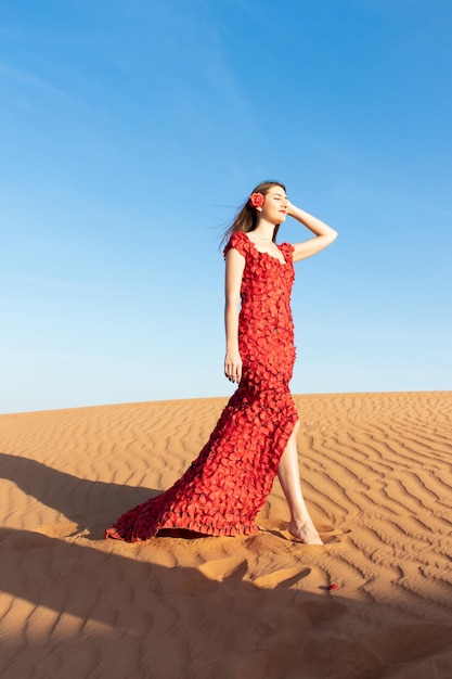 Belle jeune femme en robe longue rouge avec des pétales de rose rouges parmi le désert conception rose du désert