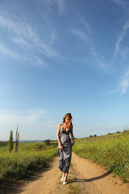 Belle jeune femme en robe marchant sur la route