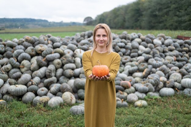 Belle jeune femme en robe moutarde avec citrouille orange en plein air sur patch. Thanksgiving ou Halloween.