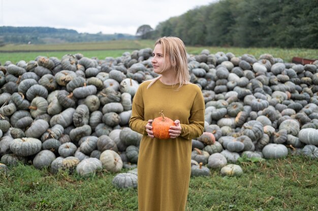 Belle jeune femme en robe moutarde avec citrouille orange en plein air sur patch. Thanksgiving ou Halloween.