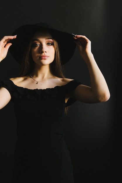 Belle jeune femme en robe noire et chapeau sur fond noir