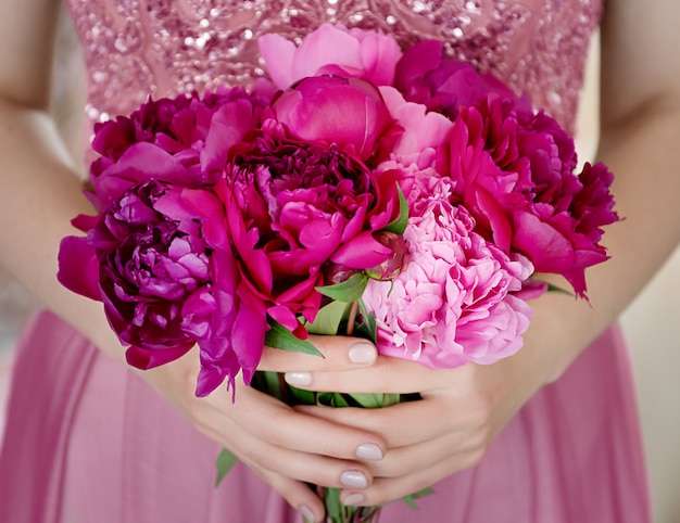 Belle jeune femme en robe rose tenant un bouquet de fleurs de pivoine dans ses mains