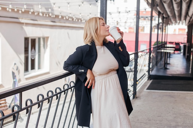 Belle jeune femme en robe et veste se promène dans la ville et boit du café