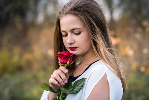 Belle jeune femme avec une rose rouge posant à l'extérieur