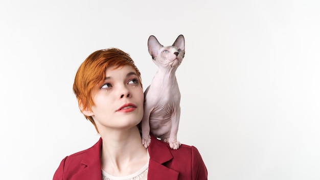 Belle jeune femme rousse hipster regardant vers le haut et chaton Sphynx ludique assis sur son épaule