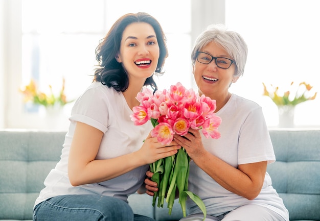 Belle jeune femme et sa mère avec des tulipes de fleurs dans les mains à la maison.